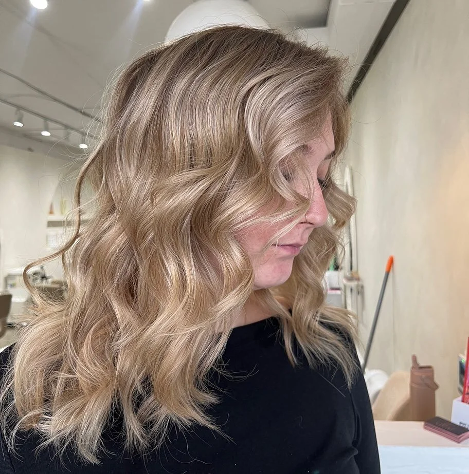 A woman with blonde, wavy hair in a salon or studio setting.
