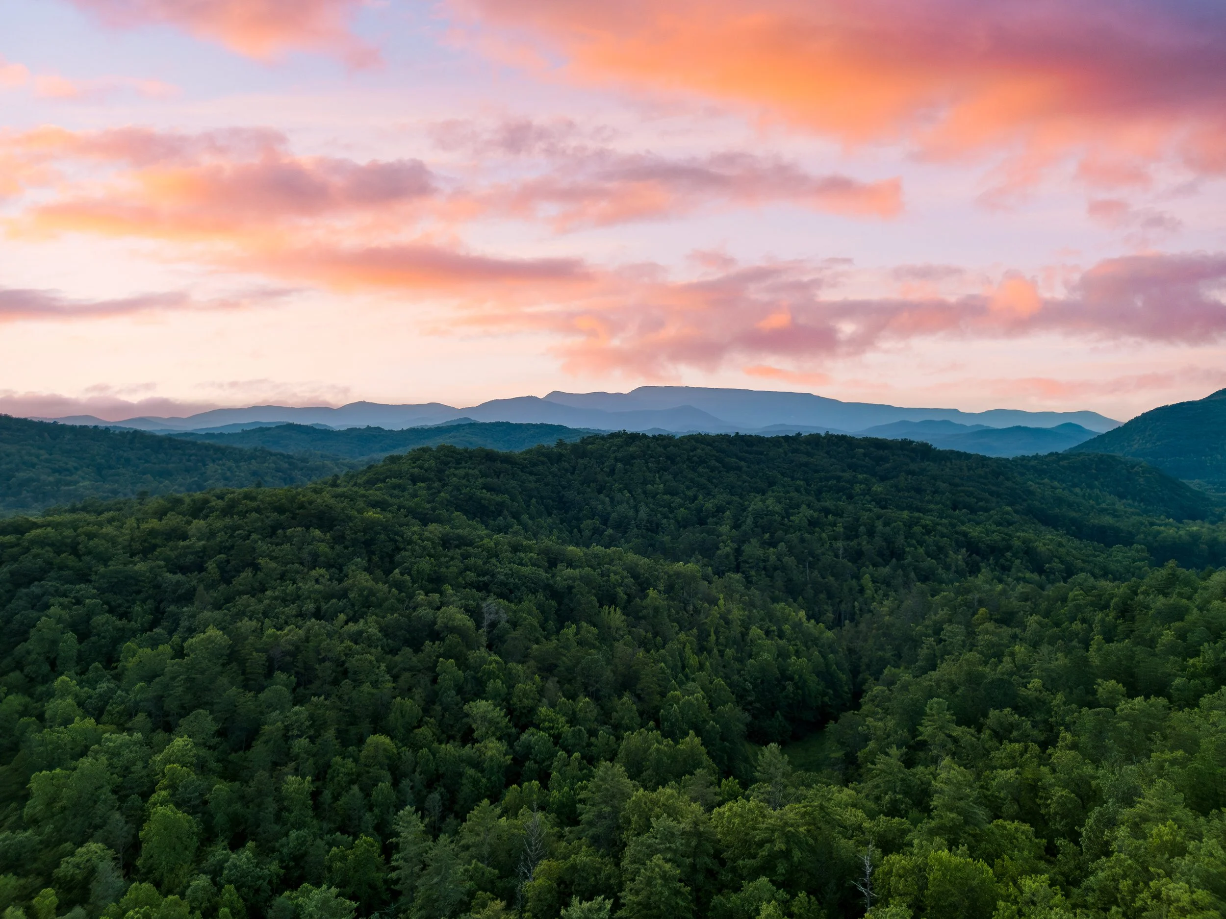 A scenic view of a mountain range with lush green forests and a colorful sunset sky with pink and orange clouds.