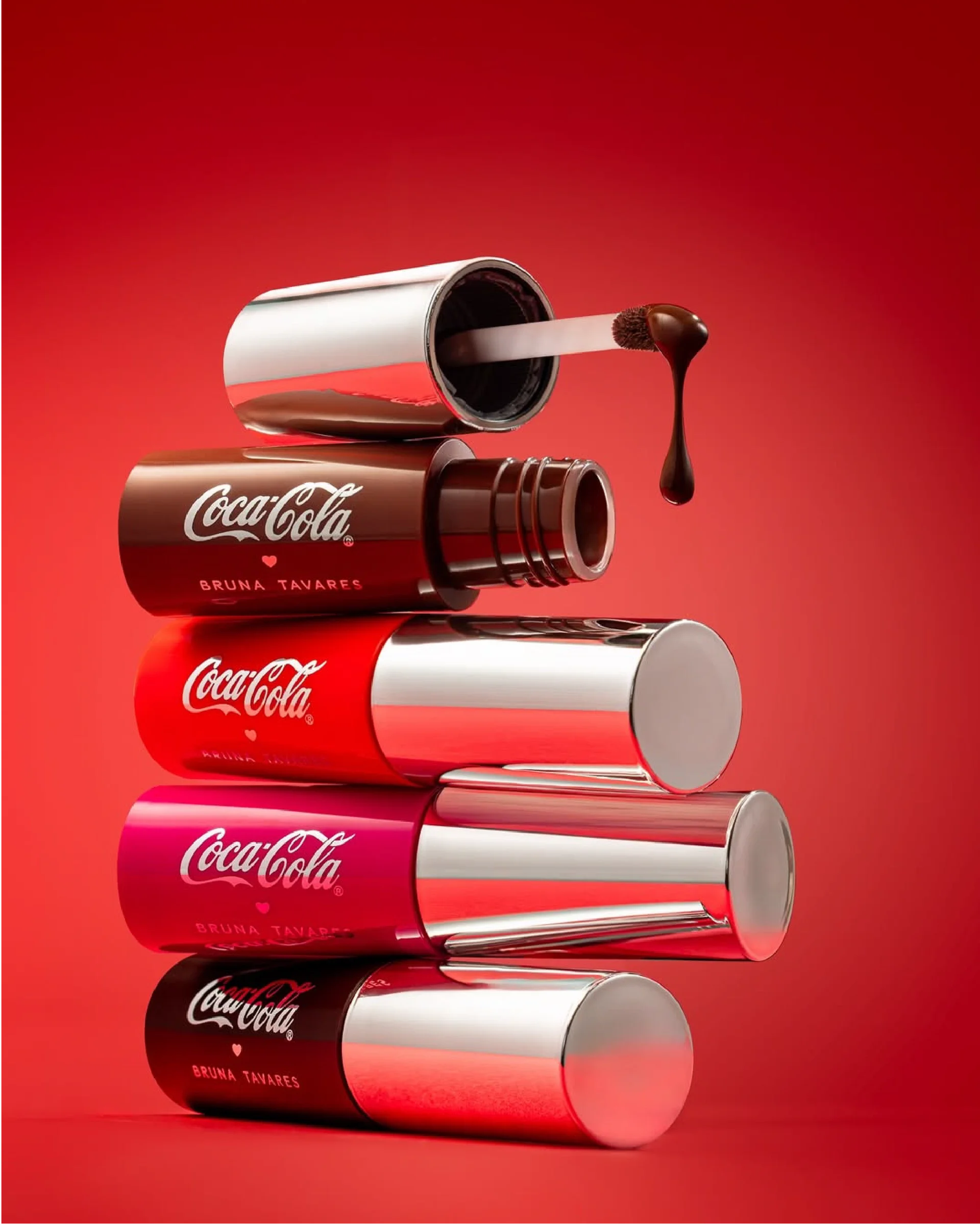 Montagem com cinco latas de refrigerante Coca-Cola empilhadas, de baixo para cima: lata preta, vermelha, rosa, prateada e uma embalagem aberta de batom com o produto derretido.