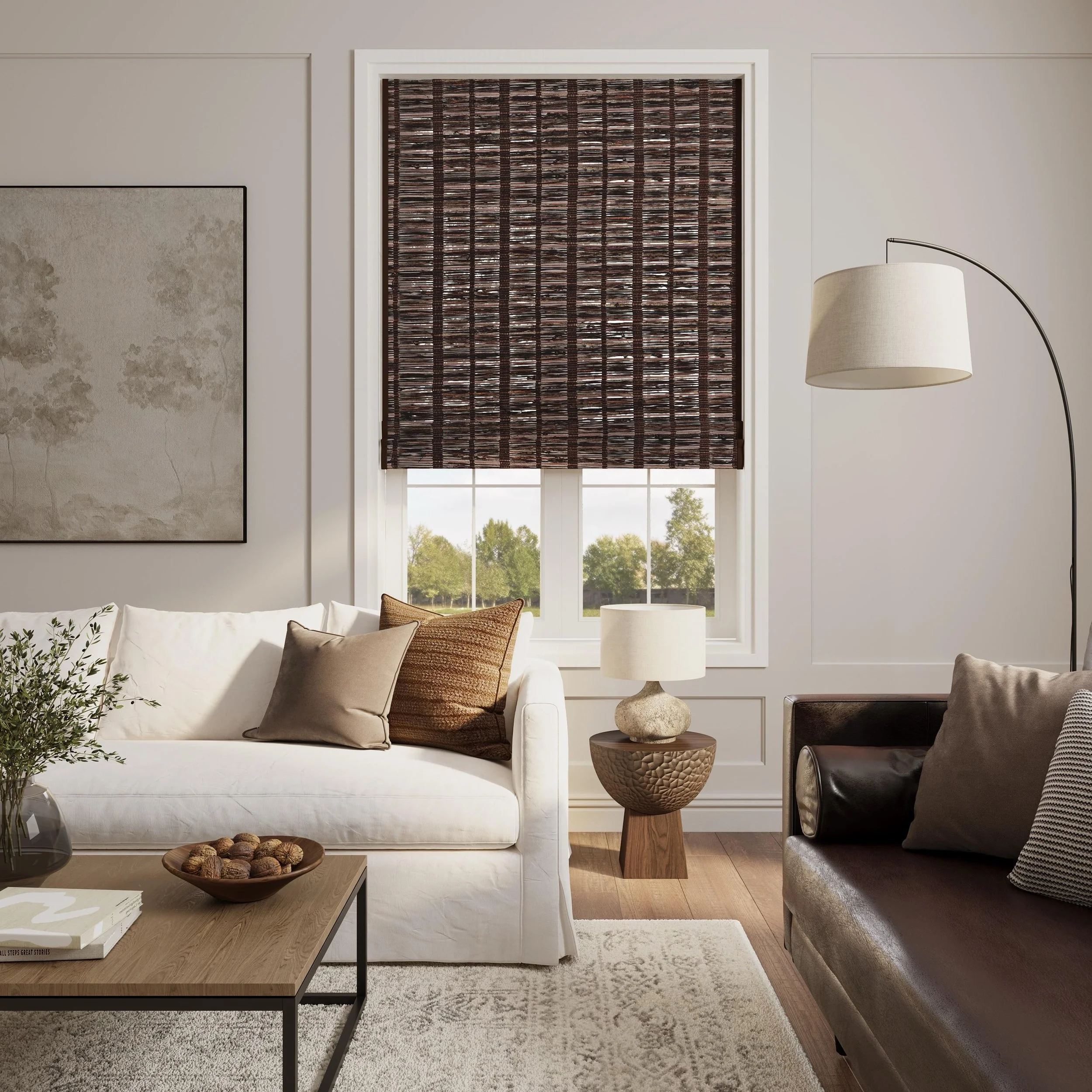 Living room with a white sofa adorned with beige and brown pillows, a wooden coffee table with walnuts and books, a bean-shaped side table, and a black leather chair. There is a large window with a patterned dark brown roller shade, a modern floor lamp with a beige shade, a framed wall art piece, and a view of greenery outside.