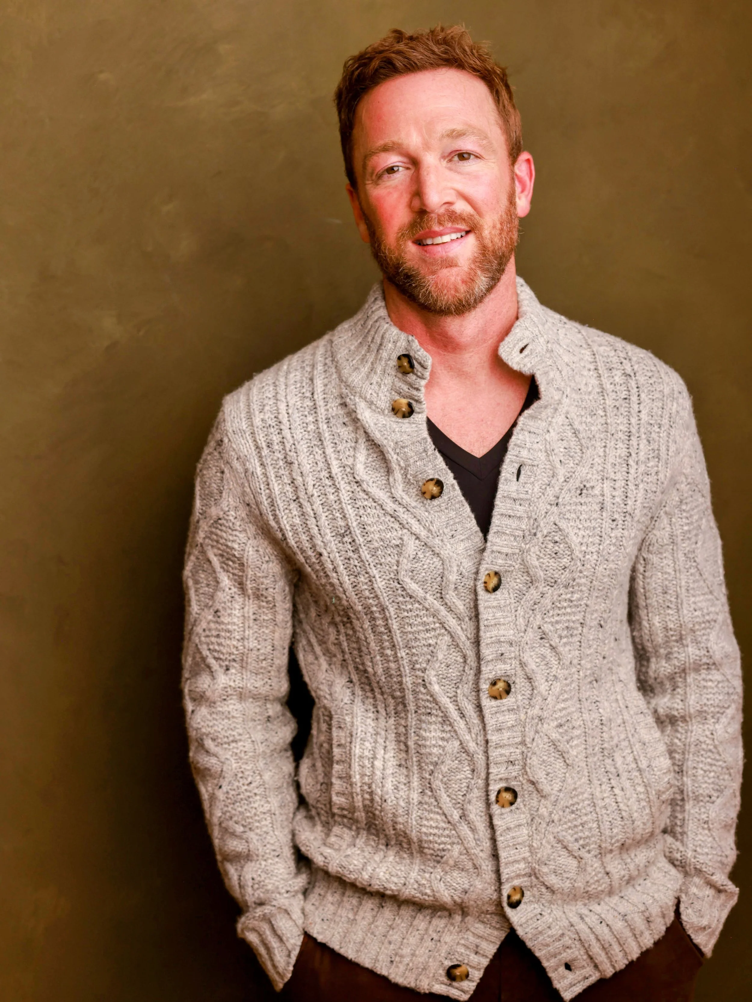 Brad Gilmore, LMFT wearing a cream-colored cable-knit cardigan with large brown buttons, standing against a plain olive-green background.