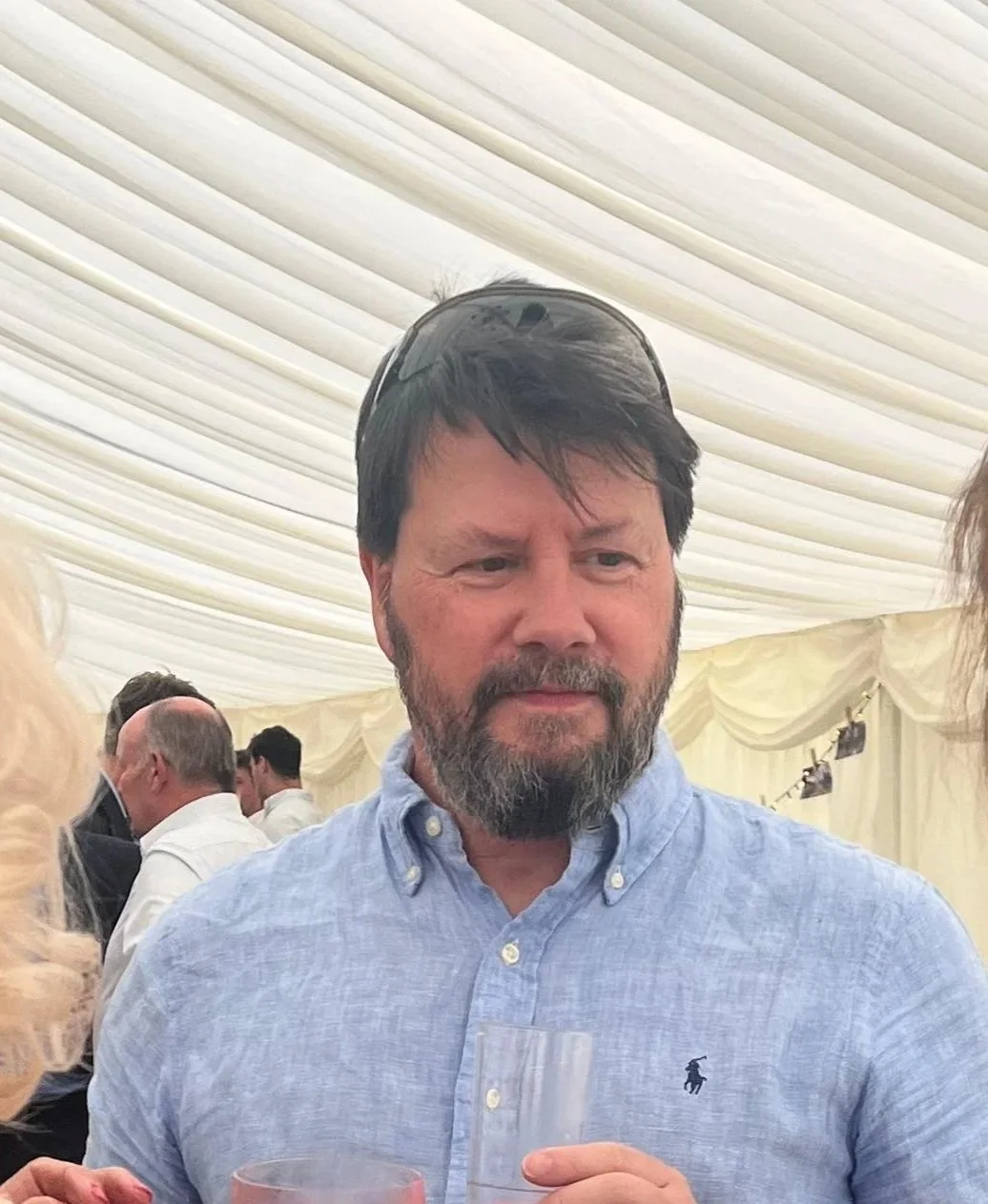 A man with a beard and dark hair wearing a light blue button-up shirt.