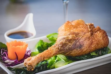 Fried chicken leg with green vegetables, purple cabbage, orange carrot, and dipping sauce on a white plate.