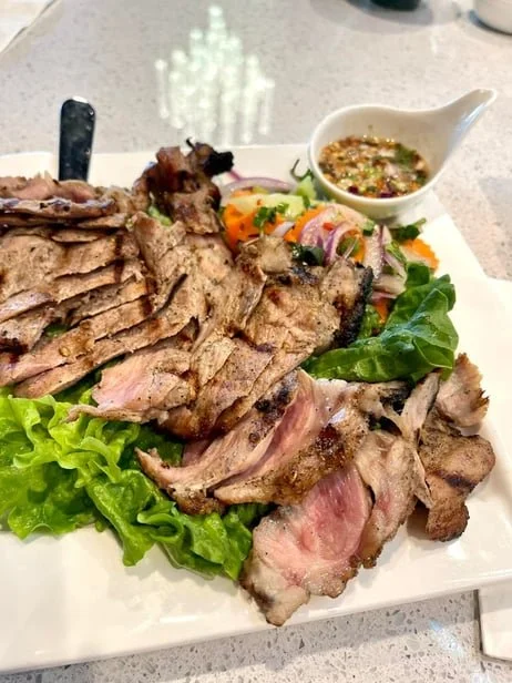A plate of sliced grilled steak with lettuce and a small bowl of dipping sauce.