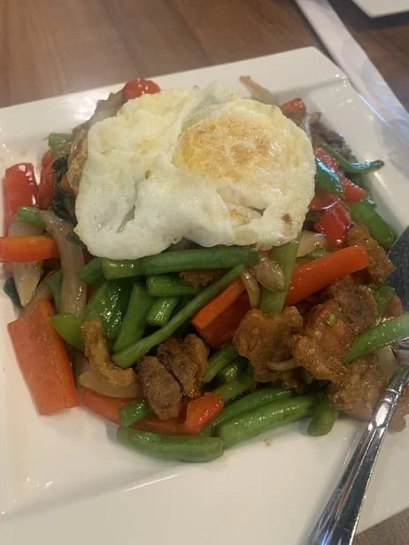 Stir-fried vegetables with carrots, green beans, and peppers topped with a fried egg on a white plate.