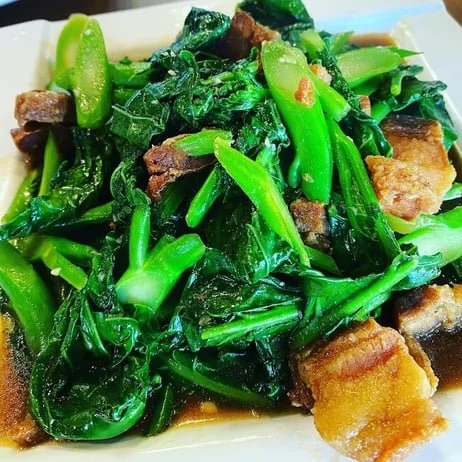A plate of stir-fried greens with pieces of pork and dark soy sauce.