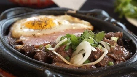 Cooked beef with green onions and a fried egg on a hot stone or skillet