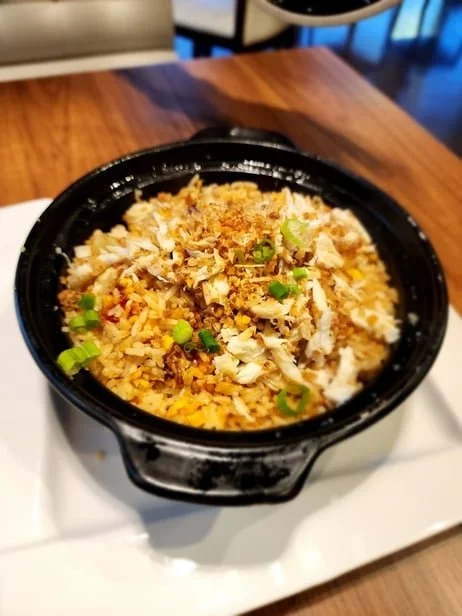 A bowl of fried rice topped with shredded chicken, green onions, and crispy fried onions.