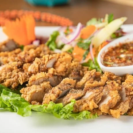 Fried chicken strips with lettuce, a small bowl of dipping sauce, shredded carrots, sliced onions, and a side salad with mixed greens and vegetables