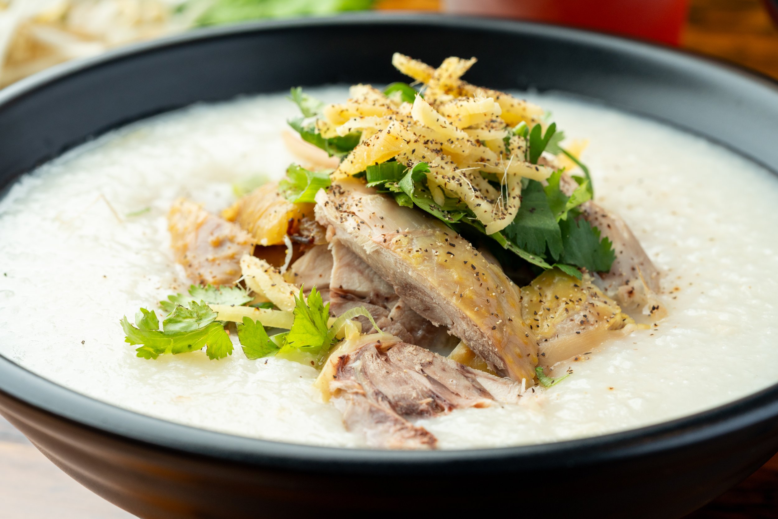 A black bowl containing cooked fish topped with shredded cheese, cilantro, sliced green onions, and crushed black pepper, served in a creamy white sauce.
