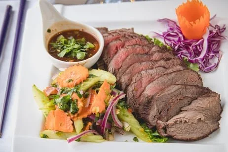 Sliced medium-rare beef with side salad and dipping sauce on a white plate
