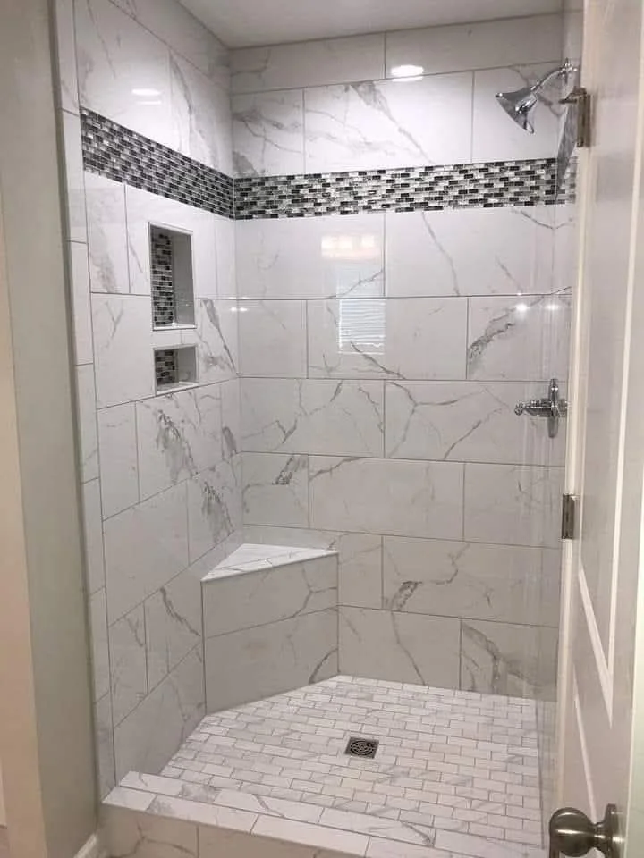 Modern shower with large white marble tiles, a horizontal strip of small mosaic tiles, a built-in niche, a bench, and a chrome showerhead.