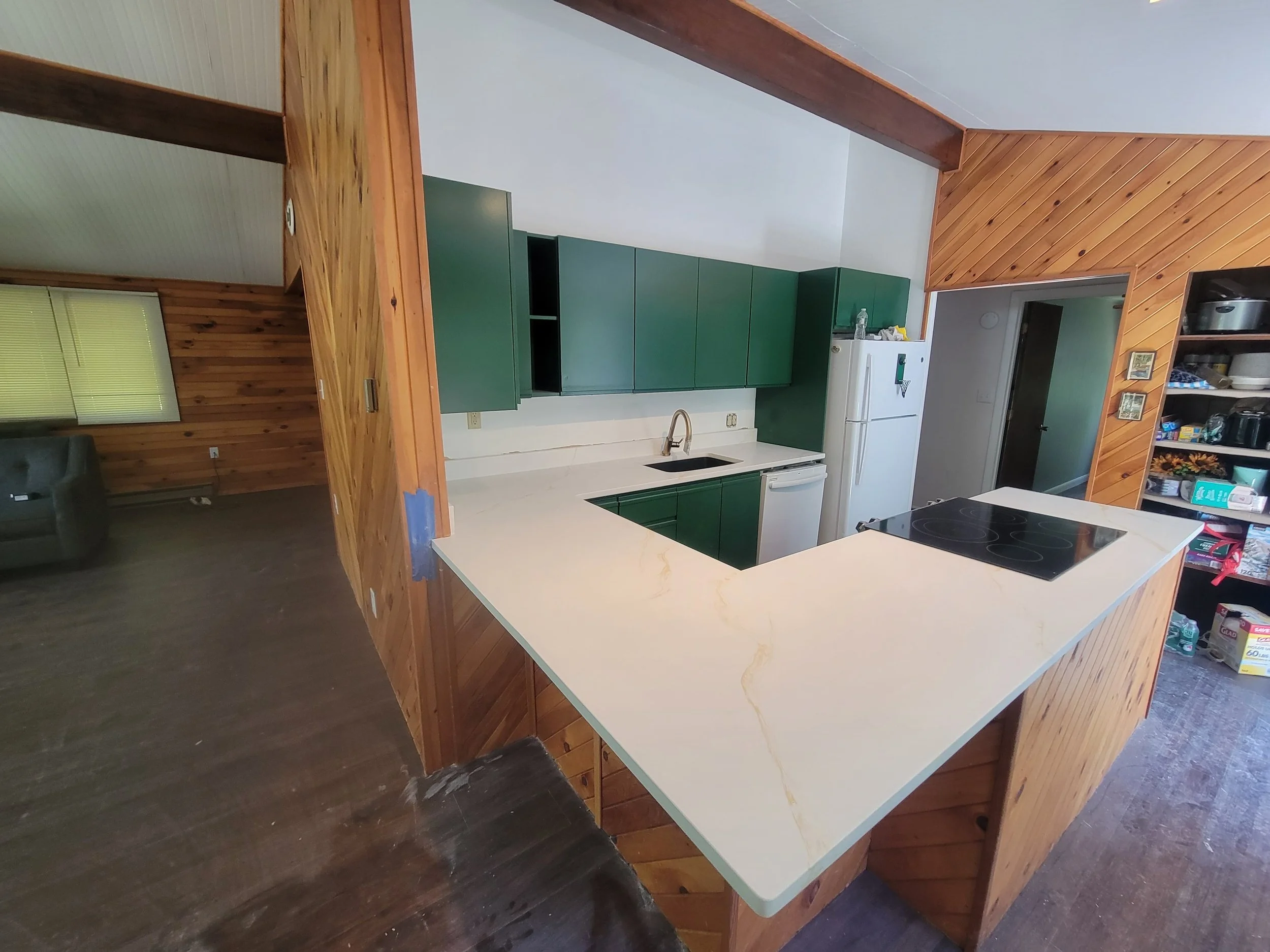 Photo of a kitchen with green cabinets, white countertop, and wooden accents, including a wooden ceiling and a large wooden island or breakfast bar.