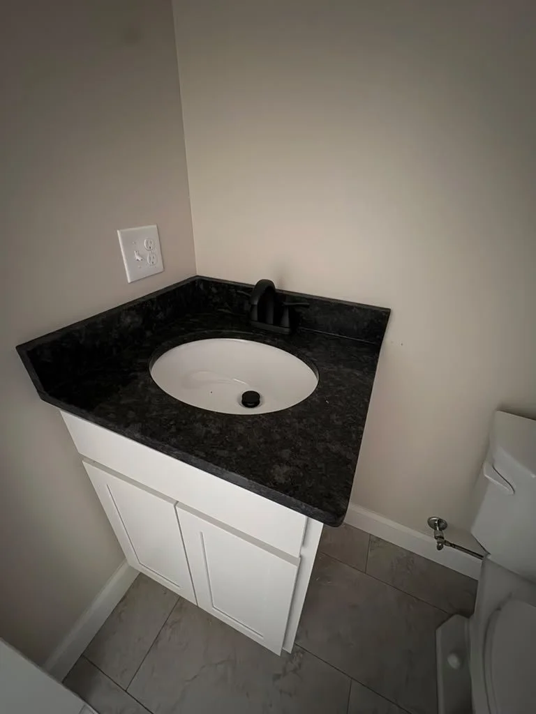 Bathroom corner with a white vanity, black granite countertop, oval sink, black faucet, and a portion of a toilet.