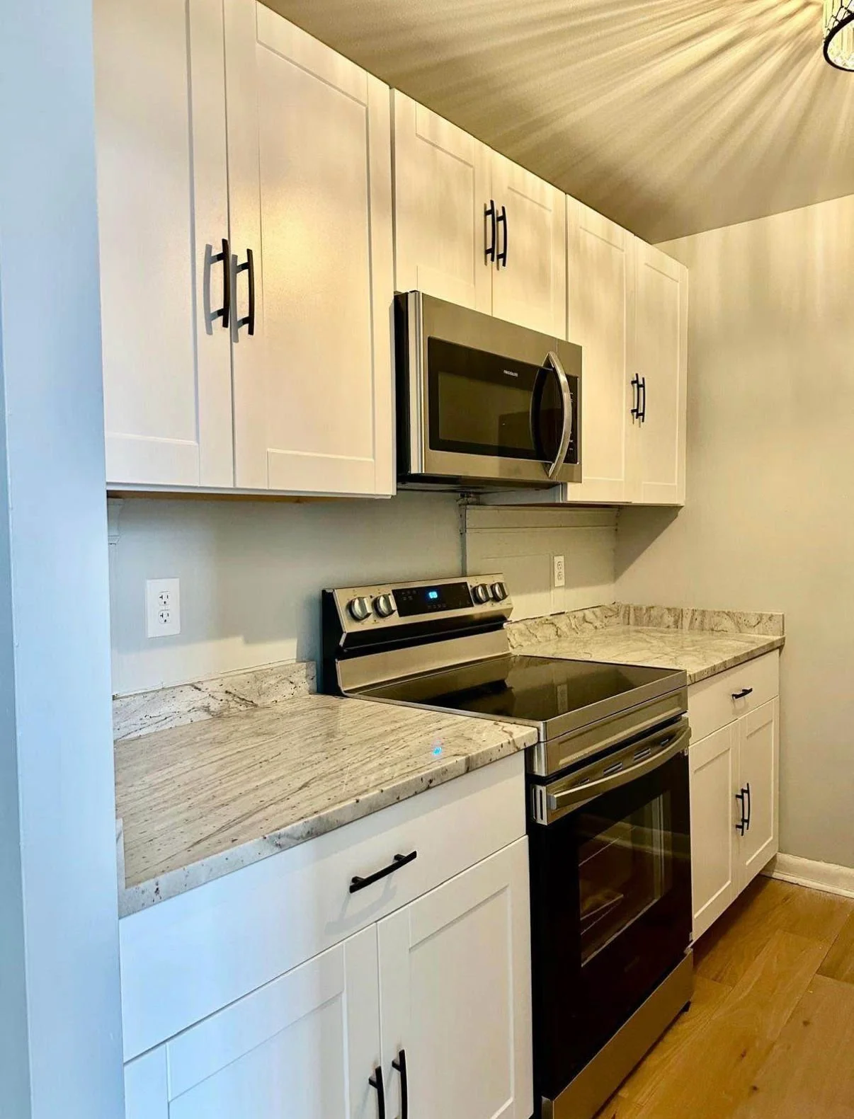 A modern kitchen with white cabinets, a marble countertop, and stainless steel appliances including a microwave, stove, and oven.
