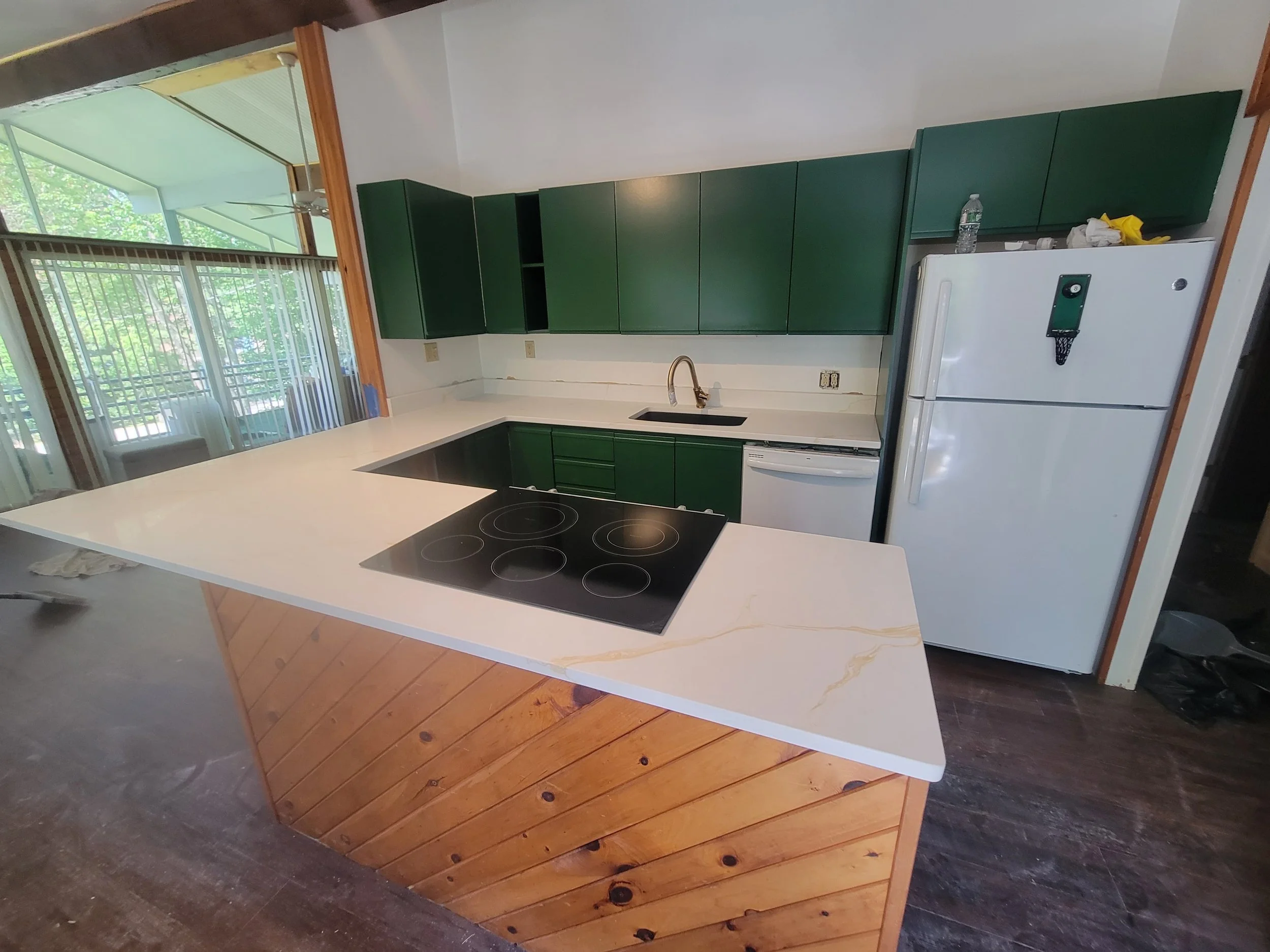 Kitchen with dark green cabinets, white countertops, a white refrigerator, and a black electric stovetop, with sliding glass doors leading to an outdoor patio.