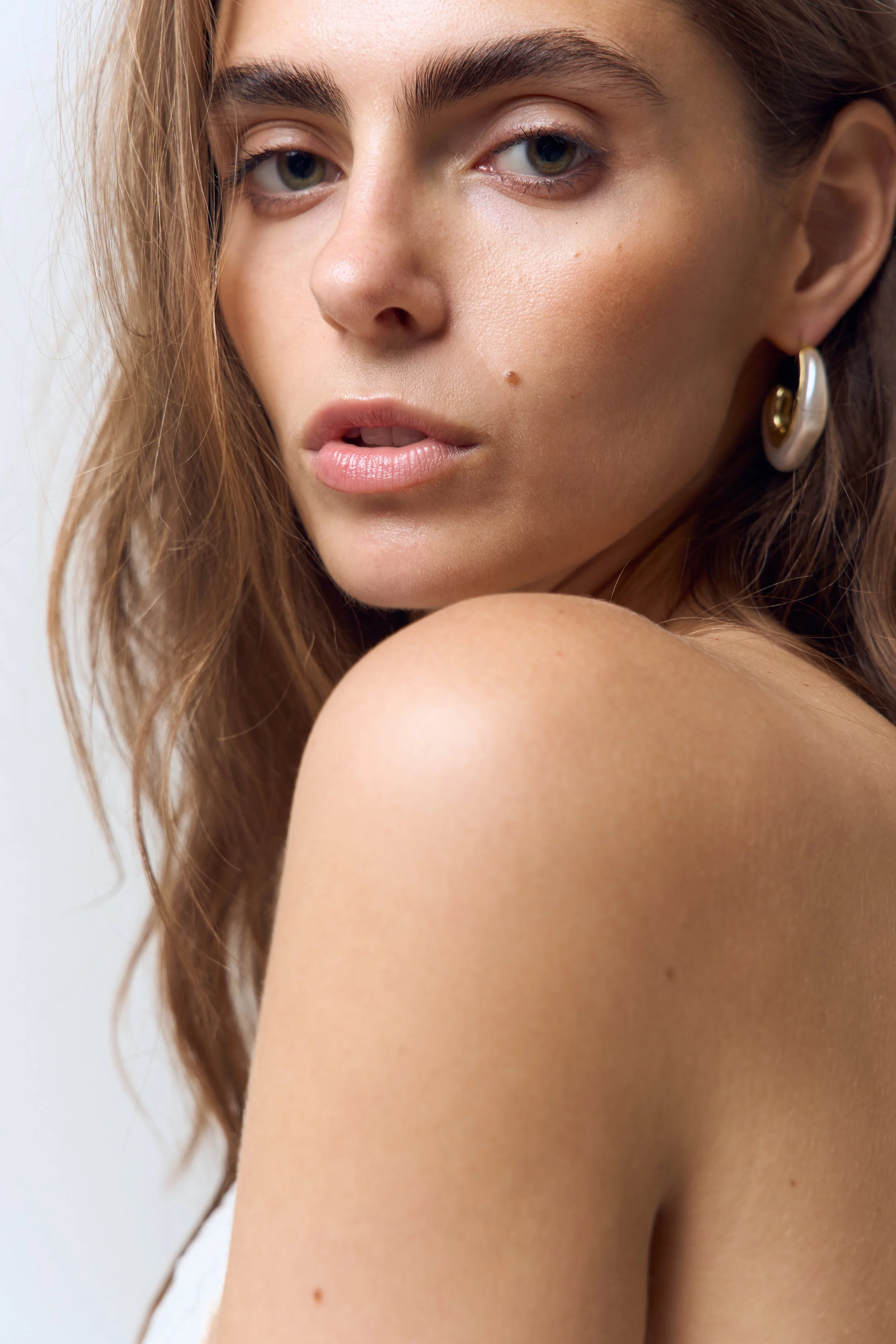 Close-up of a young woman's face with blue eyes, light skin, brown hair, and gold earrings.