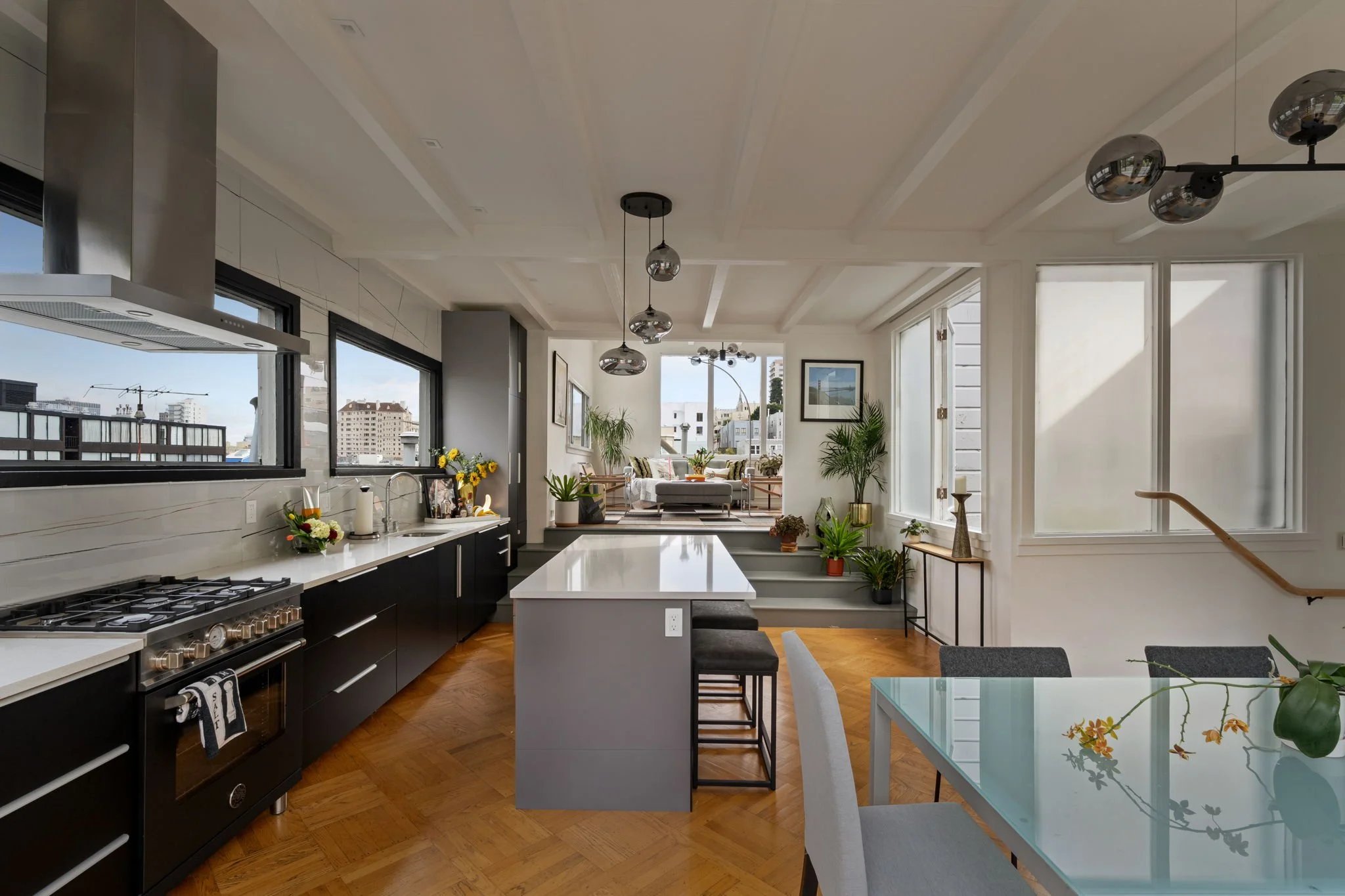 Open-concept kitchen and living room with large windows, plants, and modern decor.