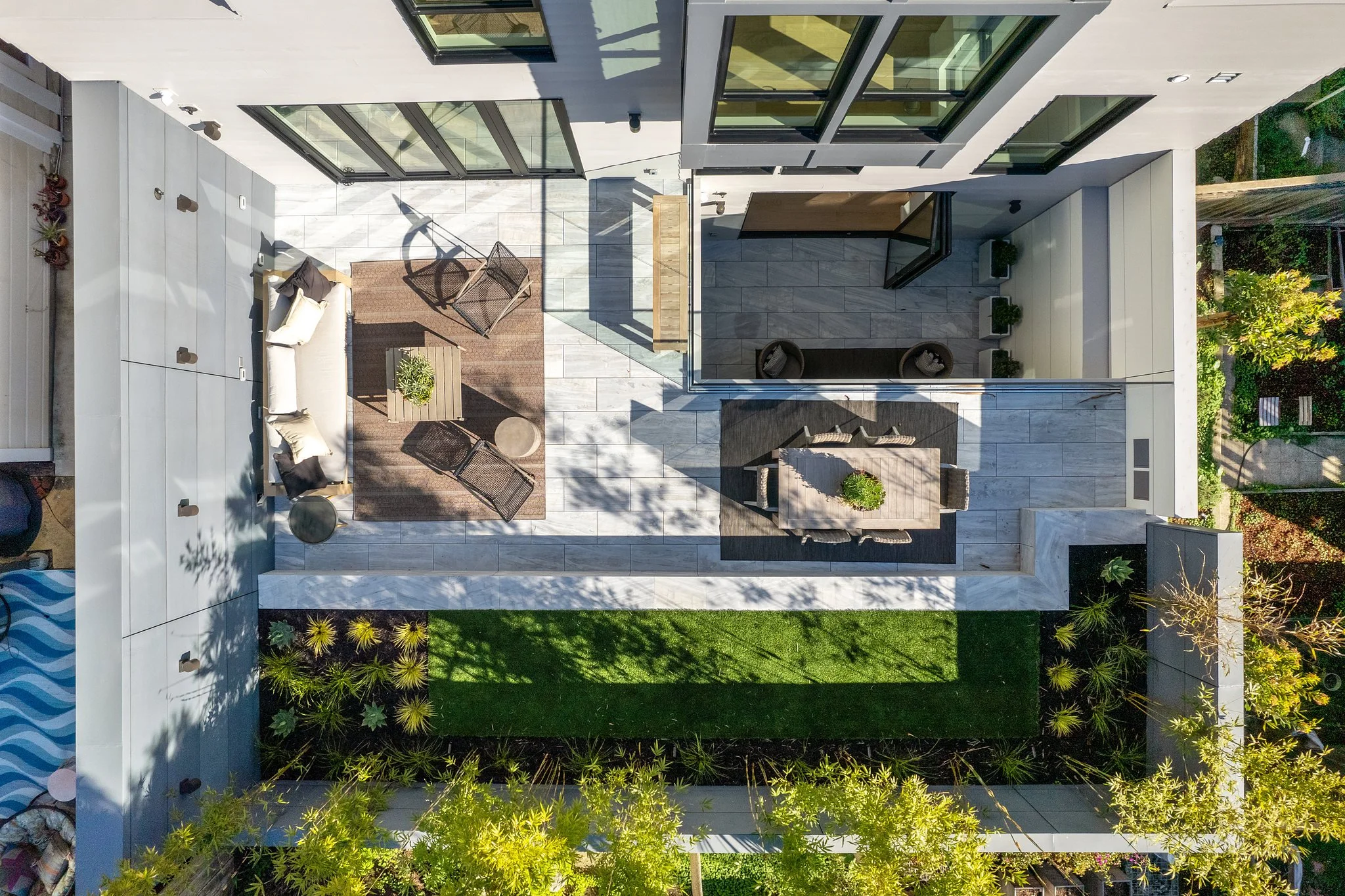 Bird's eye view of a modern outdoor patio area with seating, plants, and glass doors leading to the interior of the building, surrounded by greenery.