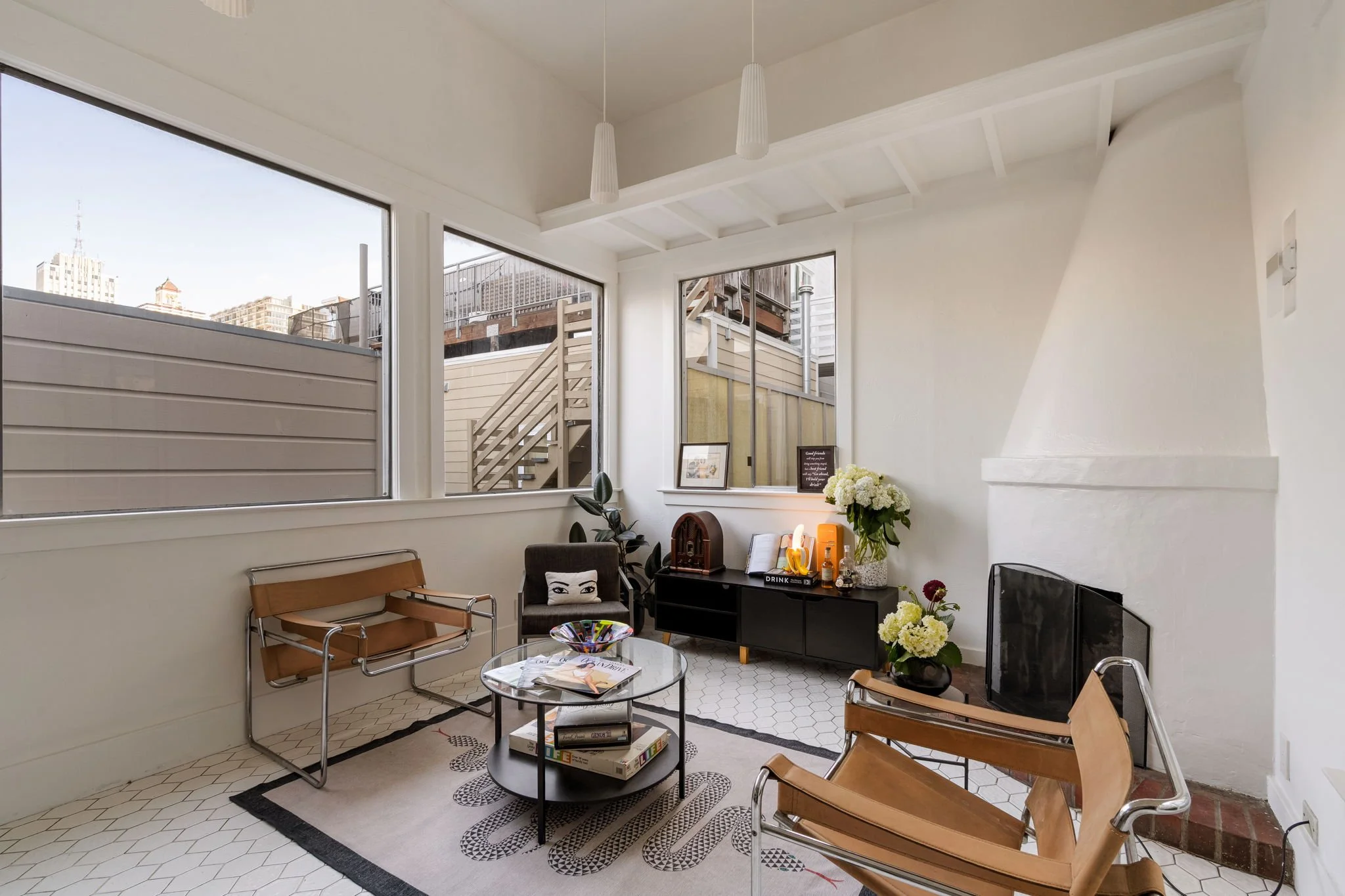 Living room with large windows, modern chairs, a black media console with decor, and a small round coffee table with books and magazines.