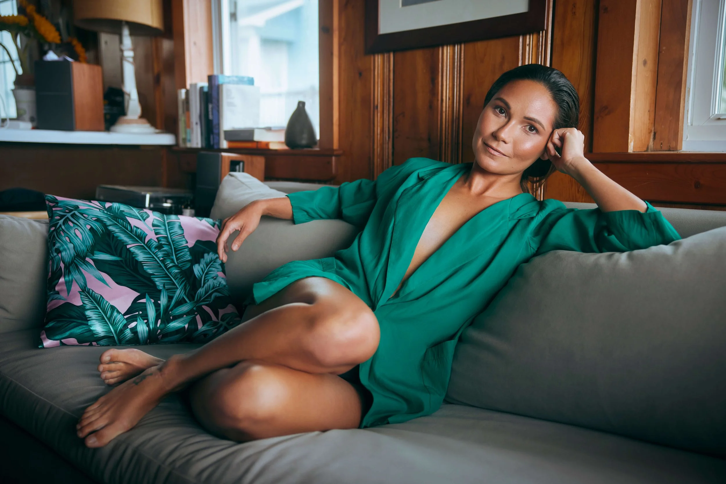 Founder, Marie Groover, is sitting on a grey couch leaning against her arm. She is wearing a green blazer against a natural wood background.
