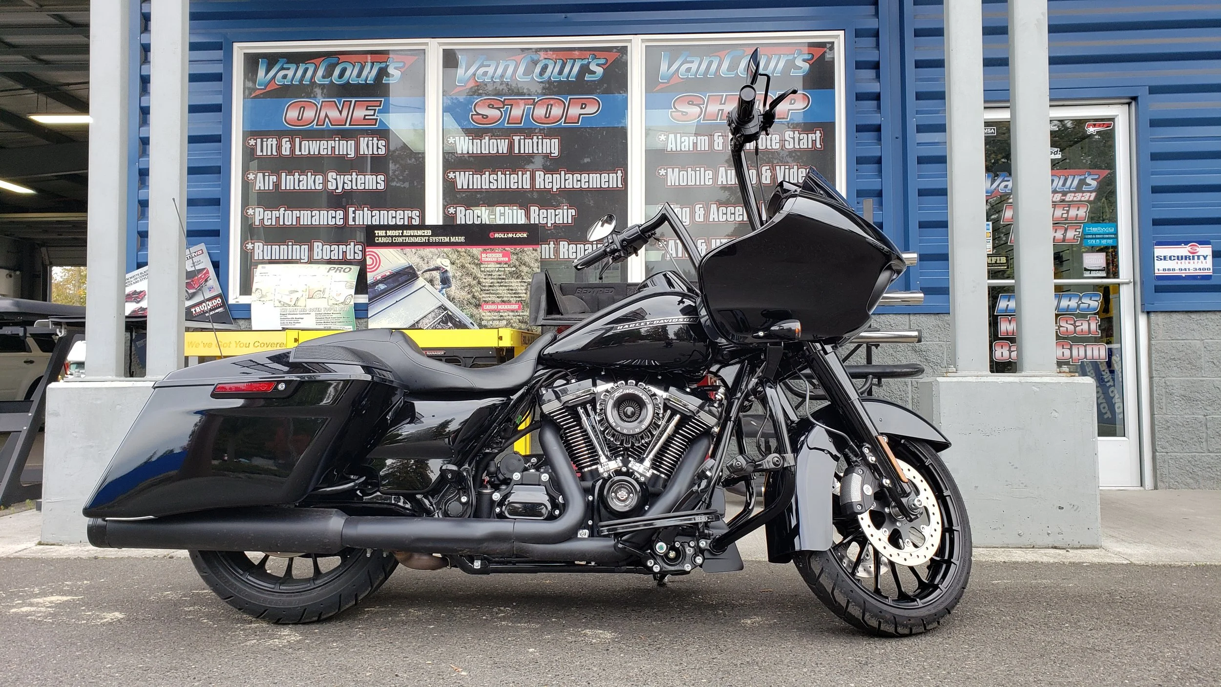 Black touring motorcycle parked in front of a blue building with promotional signs for VanCaur's automotive services.