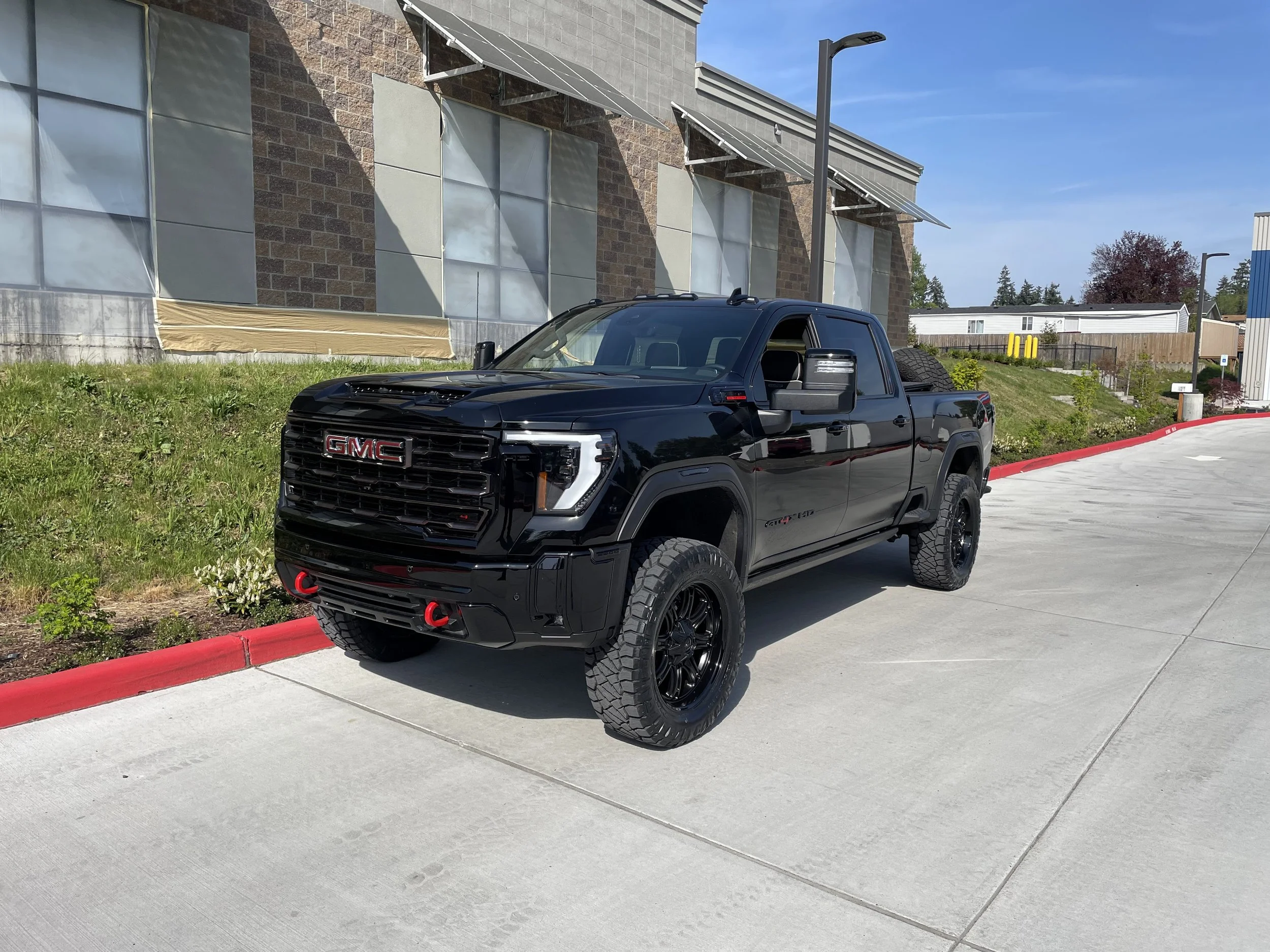 Black GMC truck parked on a sidewalk near a building under construction with scaffolding and protective coverings, against a blue sky.
