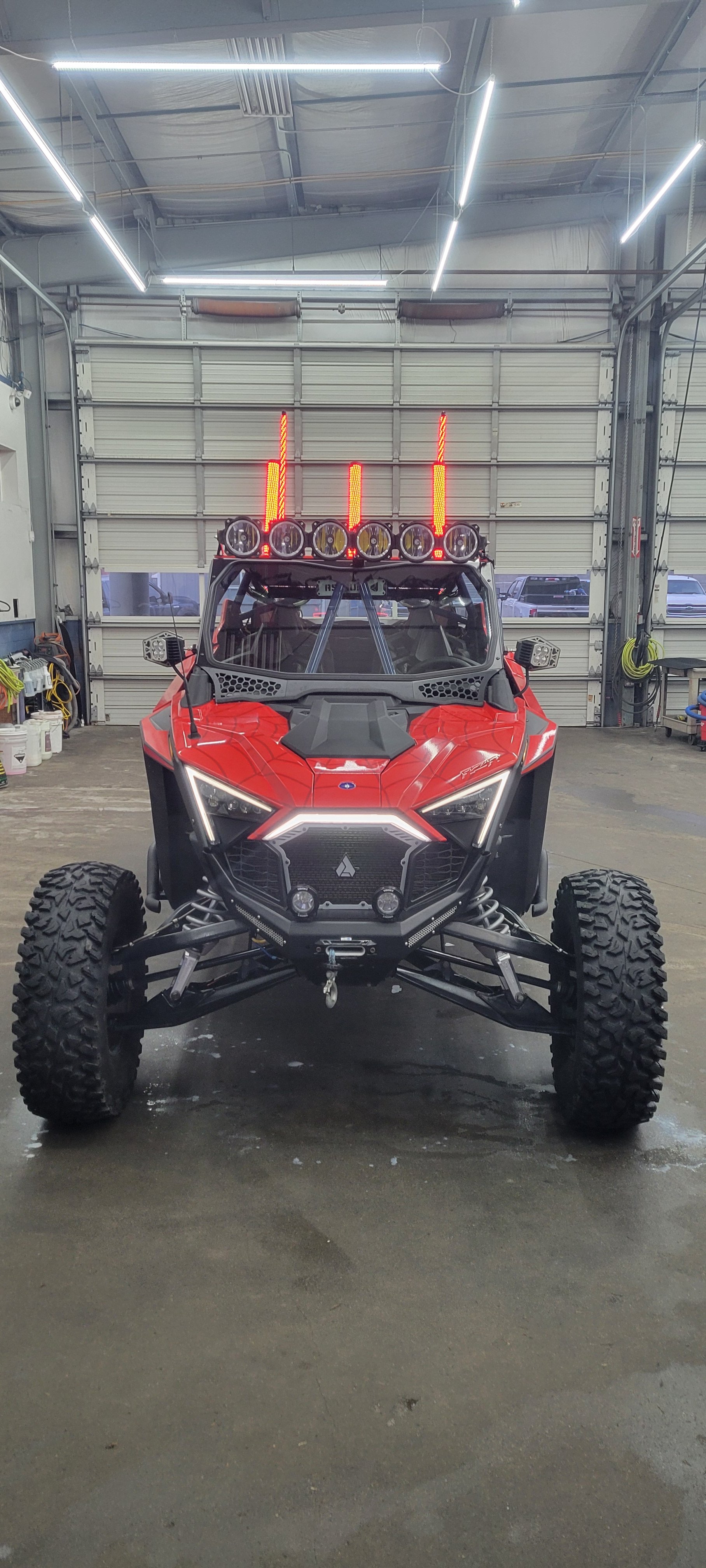 Red off-road vehicle with large tires and multiple lights on the roof, parked inside a garage.