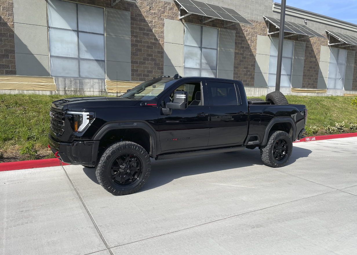 A black pickup truck parked on a sidewalk near a building with solar panels.