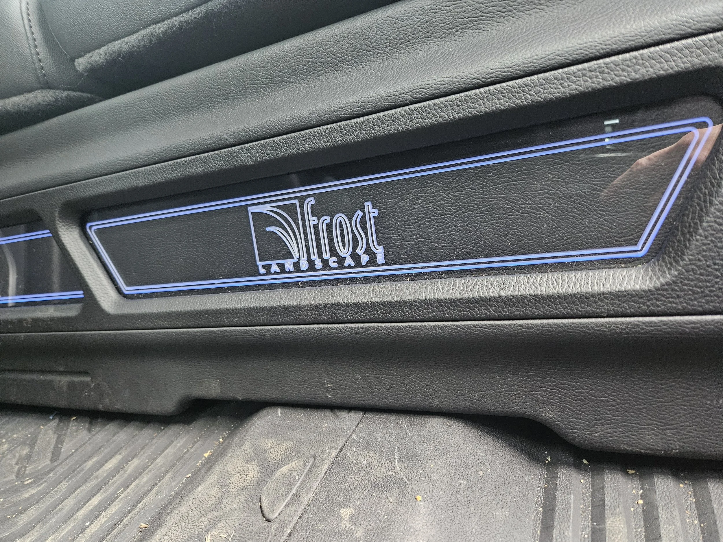 A close-up of a car dashboard with a illuminated sign that reads 'Frost Tan Escape'.