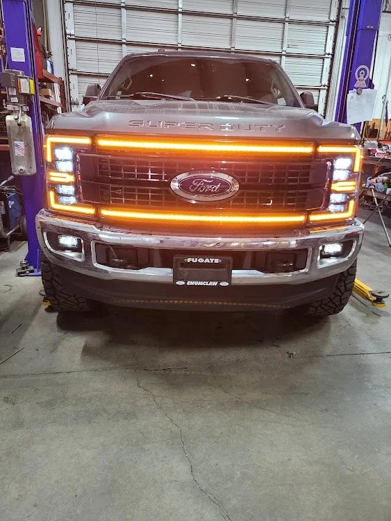 Front view of a Ford truck with distinctive orange LED light bar on the grille in a garage or workshop.