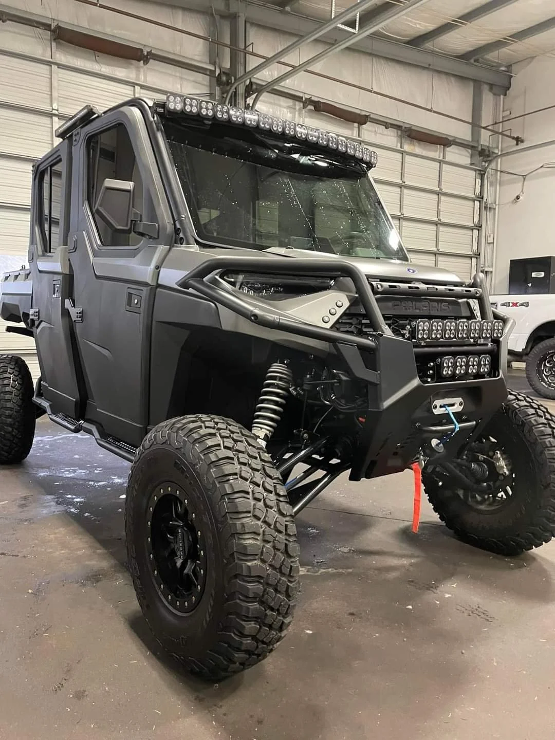 A rugged off-road vehicle with large tires, protective bars, and multiple lights, parked inside a garage.