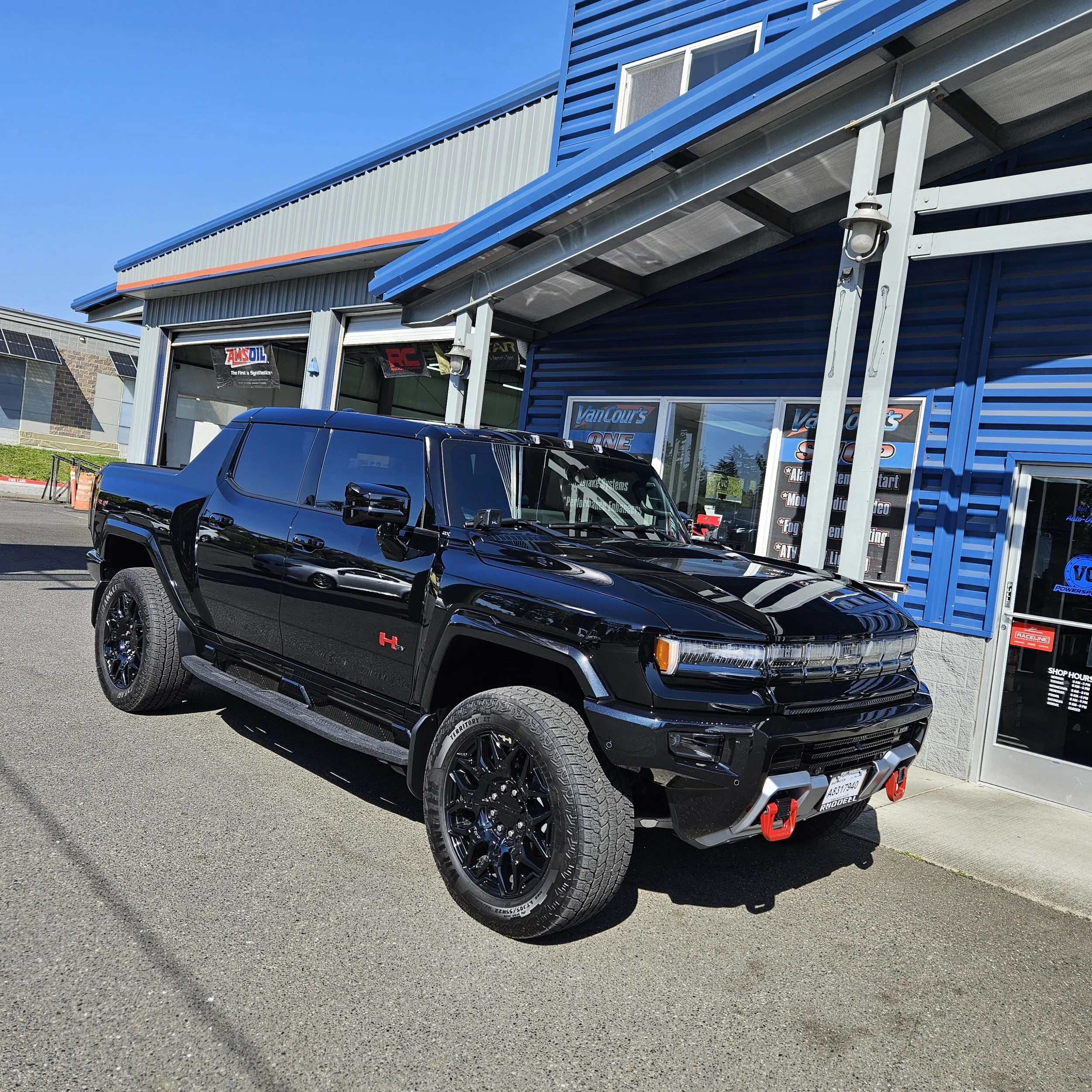 Black pickup truck parked outside a blue commercial building with large windows and a sign that reads 'VanCour's.' The building has a metal exterior with a blue and gray color scheme.