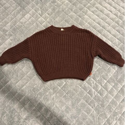 A brown knitted sweater laid flat on a quilted gray surface.