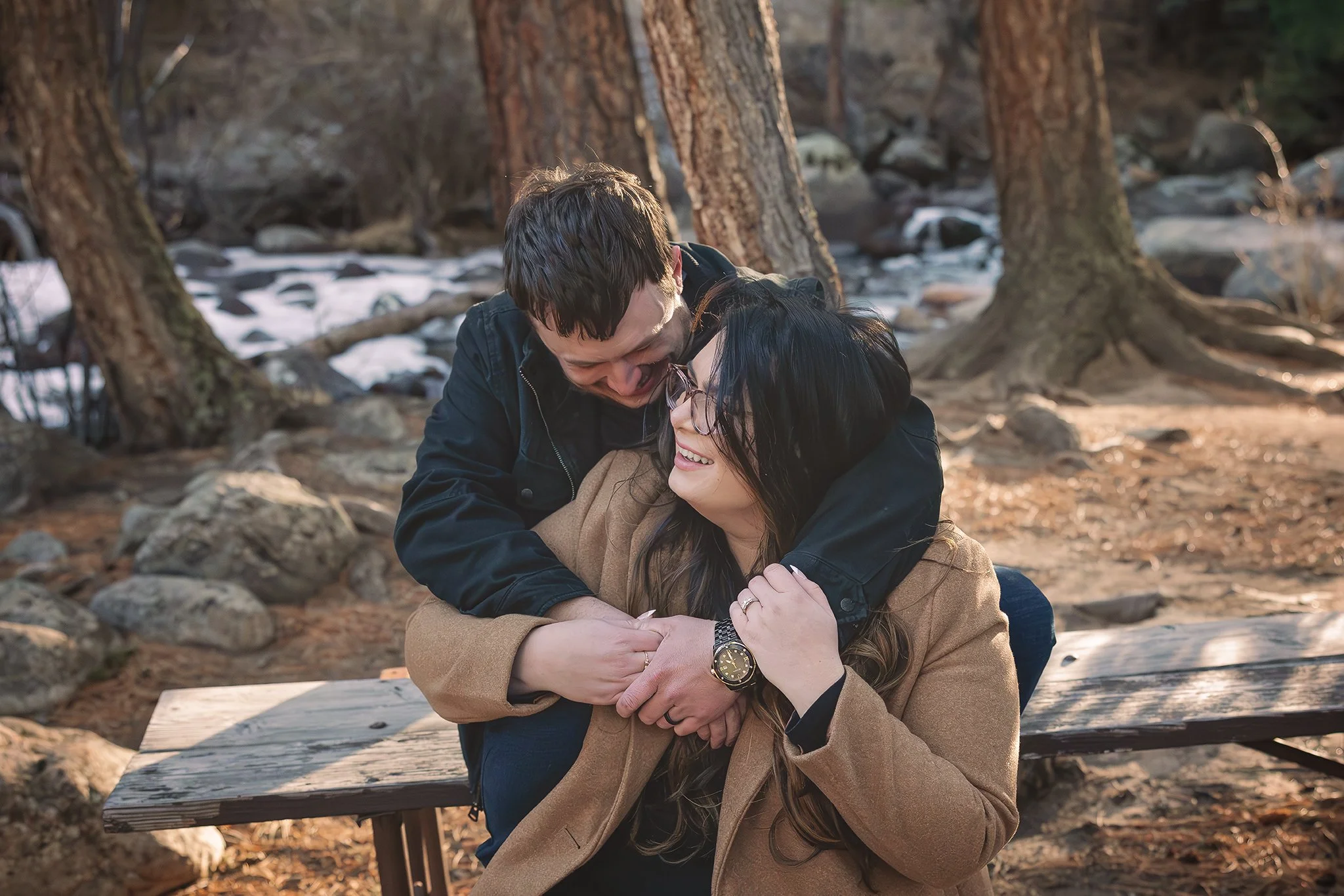 Two people hugging outdoors in a wooded area, smiling and laughing. Colorado engagement photoshoot. Winter colorado engagement photoshoot. Golden hour engagement photoshoot in Colorado.