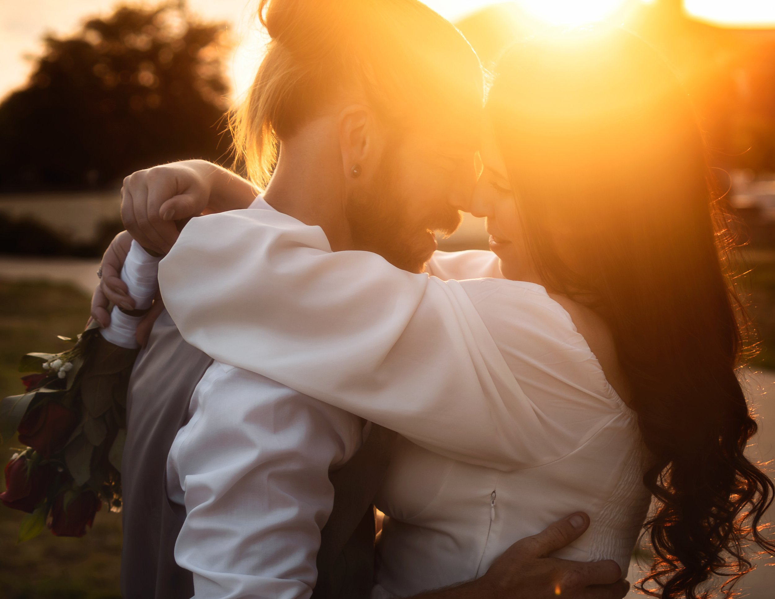 A couple embraces outdoors at sunset, with the sun glowing brightly behind them, creating a warm, romantic scene. Golden hour elopement. Colorado engagement photoshoot. Colorado elopement photographer. Greeley Colorado