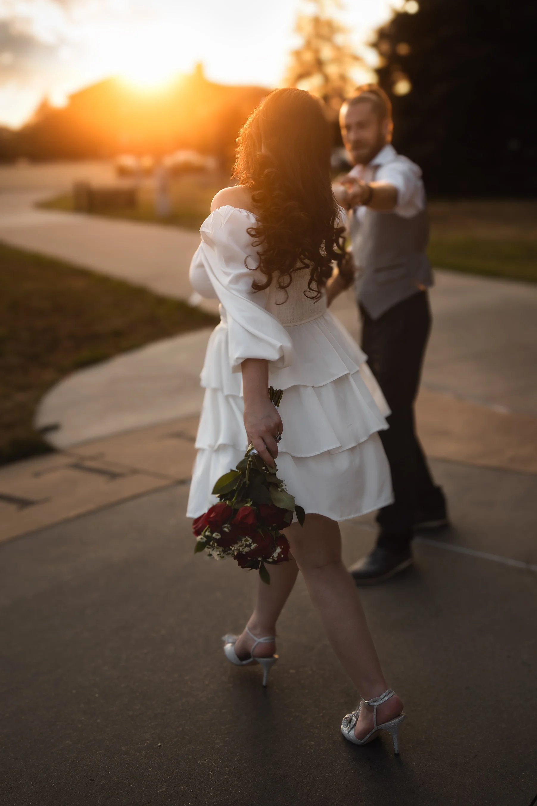 A bride in a white dress and high heels holding red roses, dancing with her husband at golden hour. Golden hour. newly weds. courthouse wedding photos. elopement photos. Colorado elopement photographer. Storytelling photographer in Colorado.