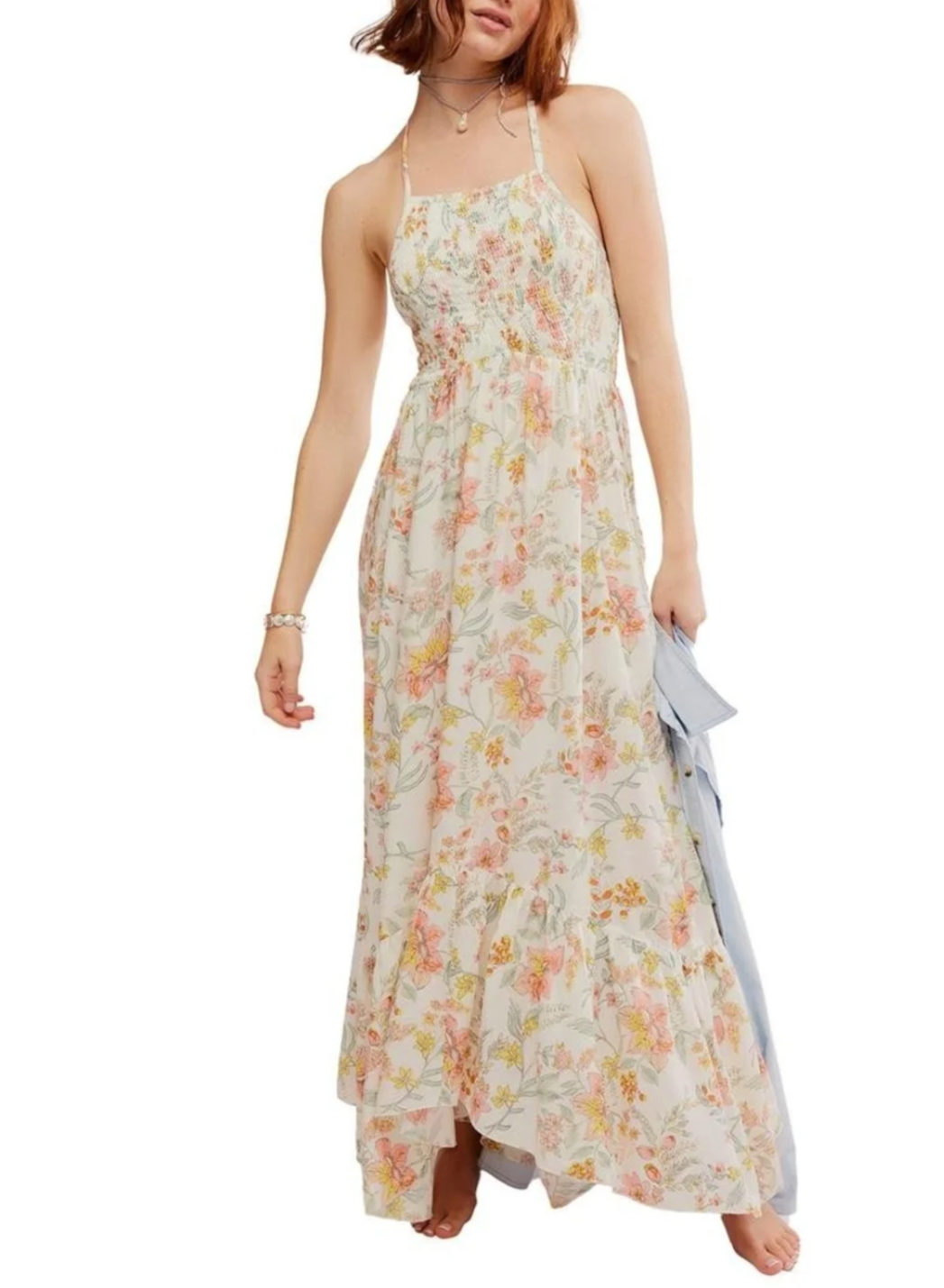 Woman wearing a floral maxi dress with spaghetti straps, holding a light blue clutch, standing against a plain background.
