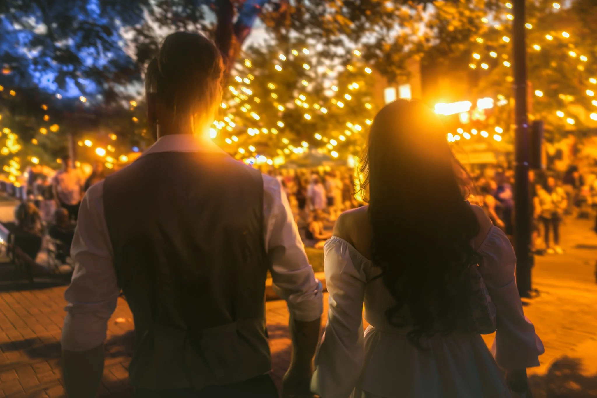 A newly wed man and a woman walking hand in hand in a downtown Greeley Colorado during dusk, with warm streetlights and trees in the background. Whimsical courthouse wedding photos in Colorado. Colorado elopement photos.