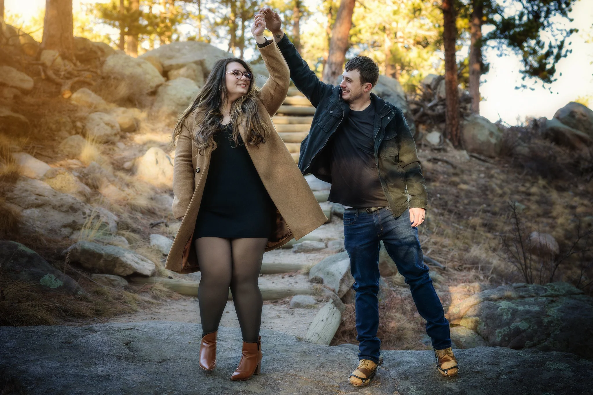 A man and woman dancing together outdoors on a rocky trail in a forested area during fall. Colorado engagement photoshoot. Colorado engagement photographer. Colorado storytelling photographer. Estes Park Photographer. Colorado Photographer.