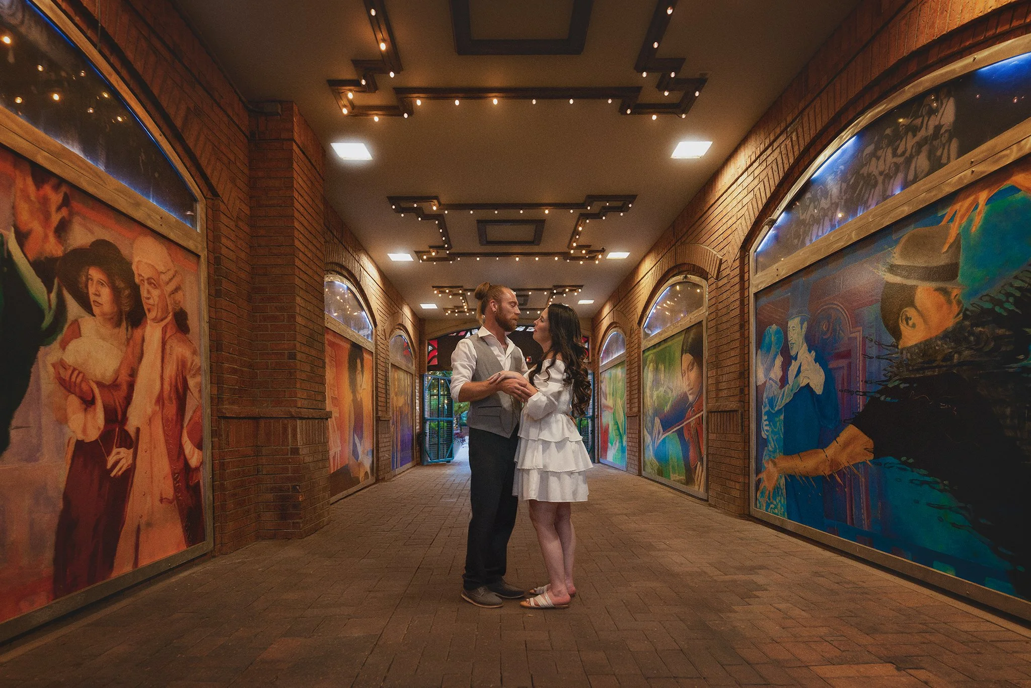 A couple dressed in wedding attire standing close together and gazing at each other in an art gallery with brick walls and colorful murals. Greeley Colorado Friday Fest. Colorado engagement photoshoot. Colorado elopement photographer. 