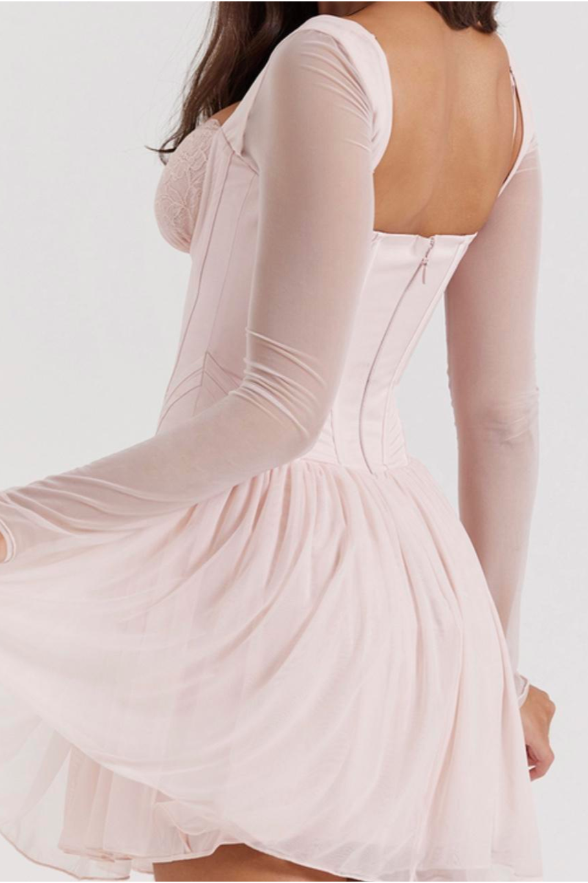 A woman wearing a pale pink, long-sleeved dress with a fitted bodice and a flared skirt, sitting with her back to the camera.