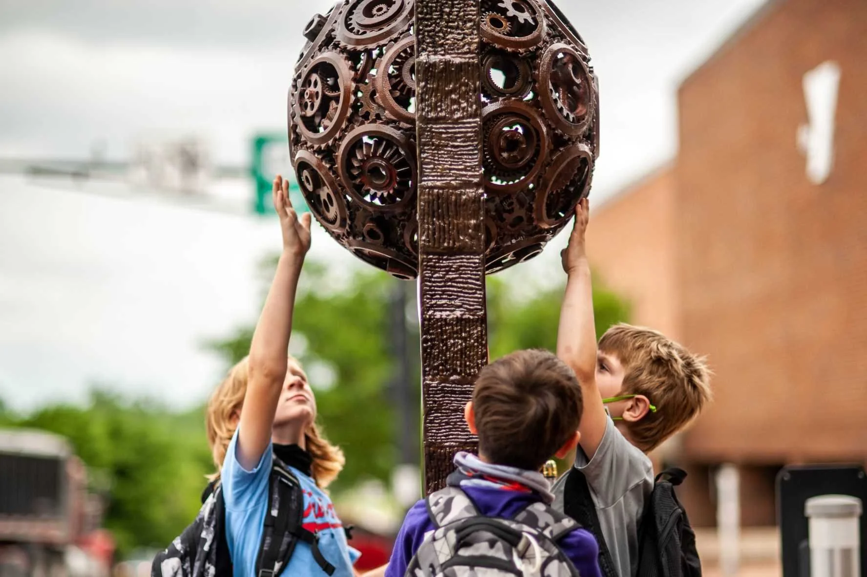 Kids reaching up to touch a bronze sculpture
