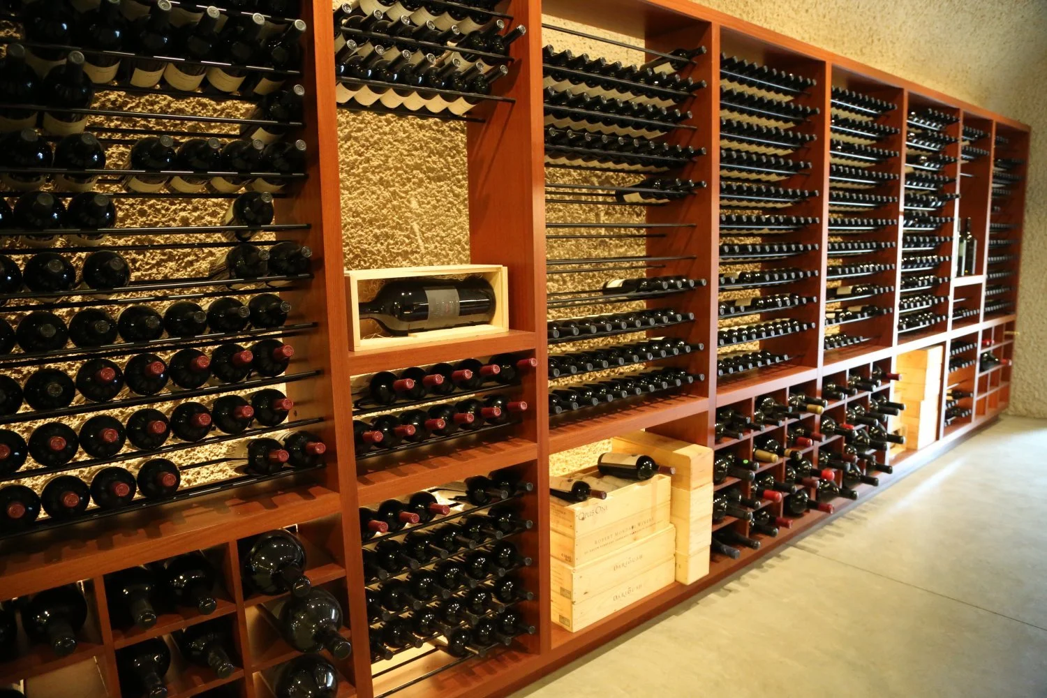 A large wooden wine rack filled with numerous bottles of red wine stored horizontally in a wine cellar or wine shop.