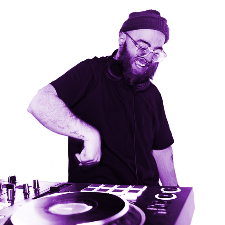 A man with glasses and a beanie smiling and dancing in front of DJ equipment.