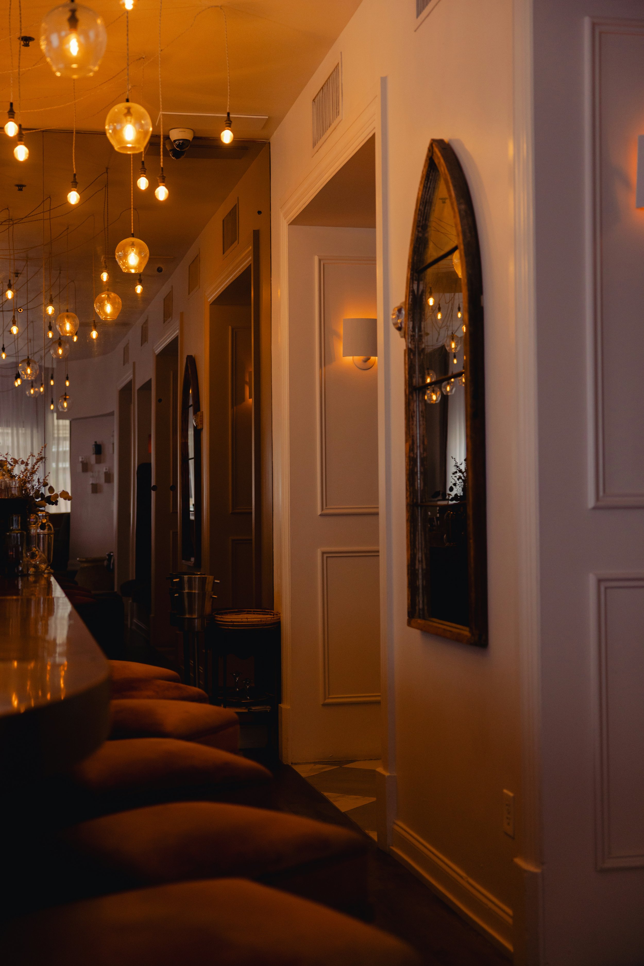 Warm lighting in a cozy interior space, featuring hanging bulb lights, wall-mounted lamps, and a reflection of lights in a mirror.