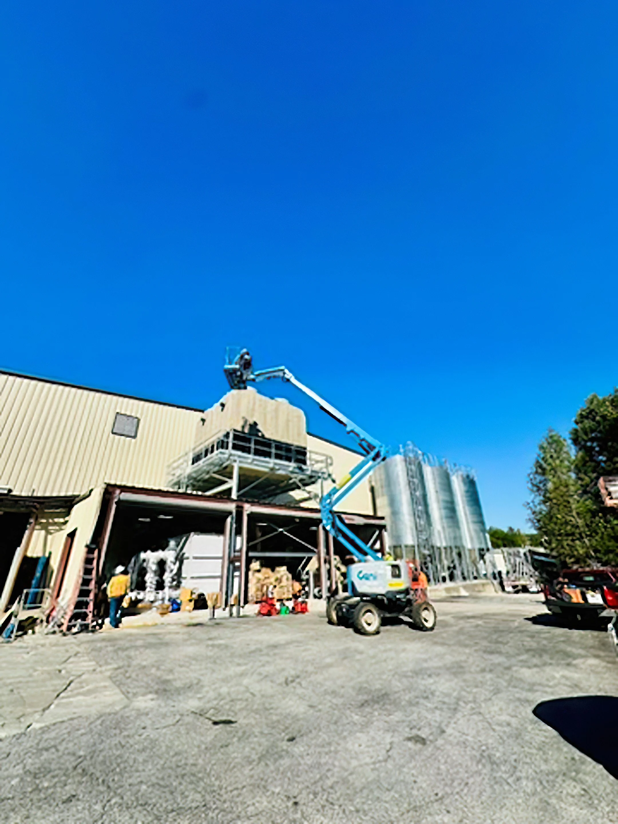 Construction site with a yellow building, a blue boom lift, a small vehicle, and construction materials, under a clear blue sky.