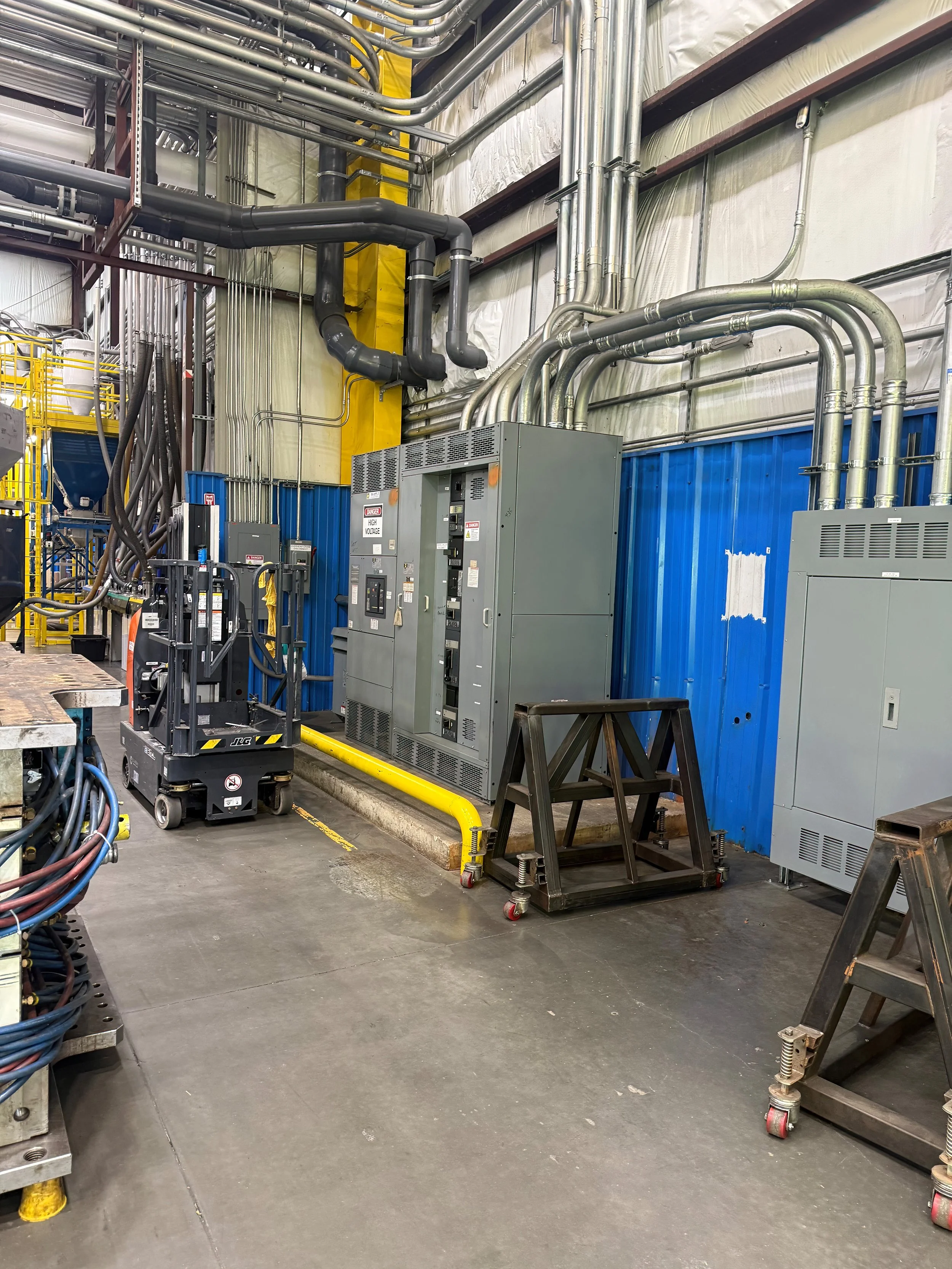 Industrial setting with pipes, electrical panels, a lift, and tools on the floor.