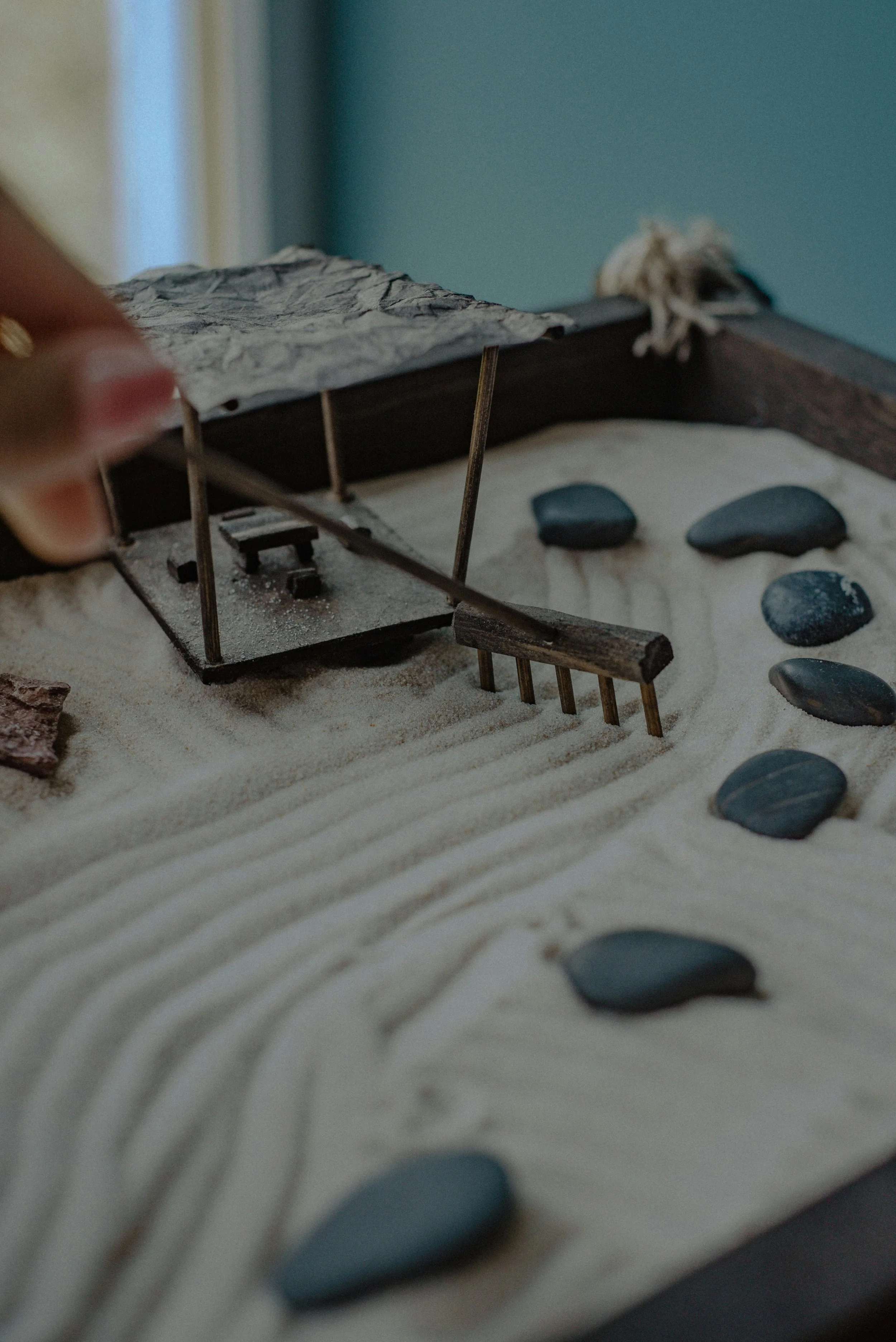 A miniature architectural model of a modern building with a flat, textured roof, supported by thin vertical columns, situated on sandy terrain with scattered black stones.