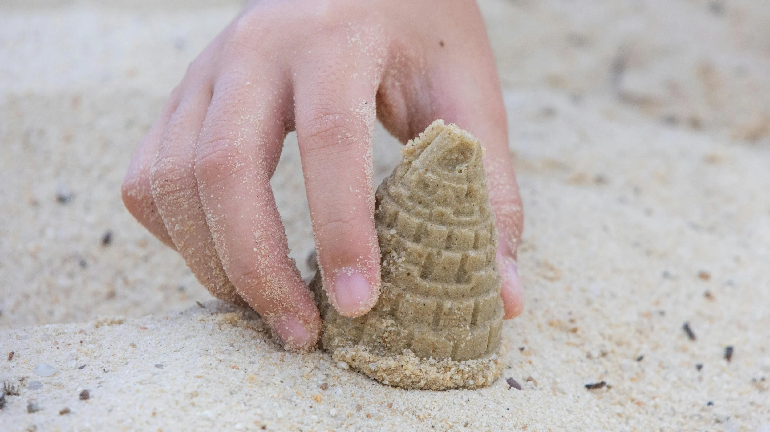 Close-up of a child's hand holding a sandcastle, with sand on their fingers.